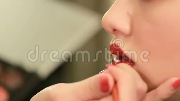 化妆师用画笔在漂亮漂亮的女人嘴唇上涂口红维萨吉斯特和年轻女孩的特写美容和化妆视频的预览图