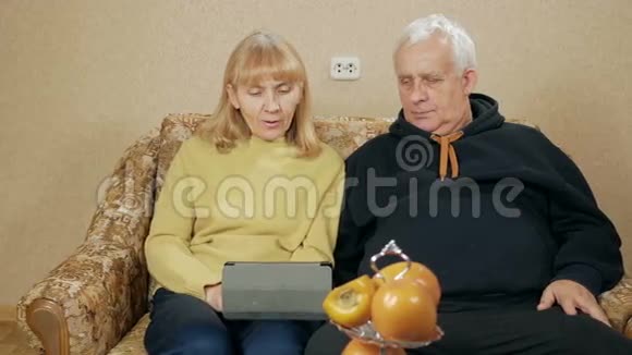 老夫妇在平板电脑上的视频链接上响起夫妻俩坐在家里的沙发上的概念视频的预览图
