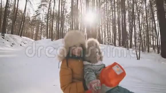 年轻的母亲和小女儿在冬天的公园里玩雪橇视频的预览图