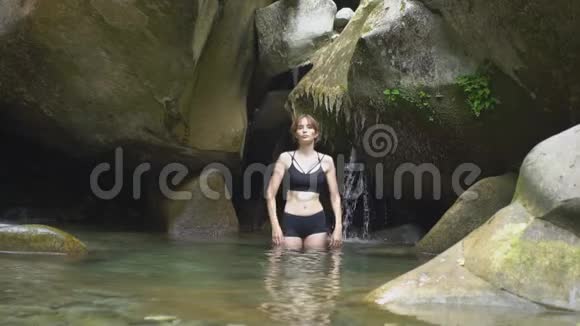 动作缓慢的年轻女子用手在绿色热带森林的山湖上溅起水花上面有小瀑布视频的预览图