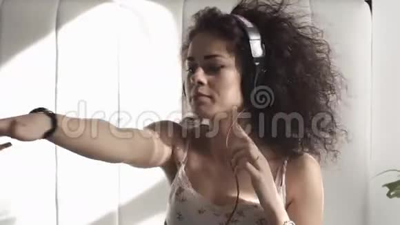 年轻女子在卧室里用耳机听音乐卷毛的女孩向她跳舞视频的预览图
