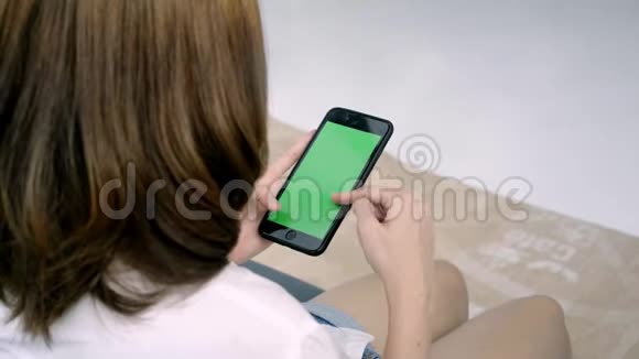 年轻的亚洲女性使用带有绿色屏幕的黑色智能手机设备视频的预览图