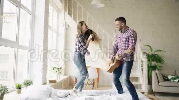 有趣的快乐和相爱的夫妇在床上跳舞用电视控制器唱歌弹吉他男人和女人在视频的预览图