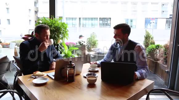 两个商人坐在咖啡桌上用手提电脑喝茶聊天视频的预览图