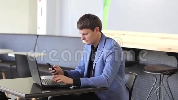 年轻的商人在咖啡馆里用电脑和电话工作视频的预览图
