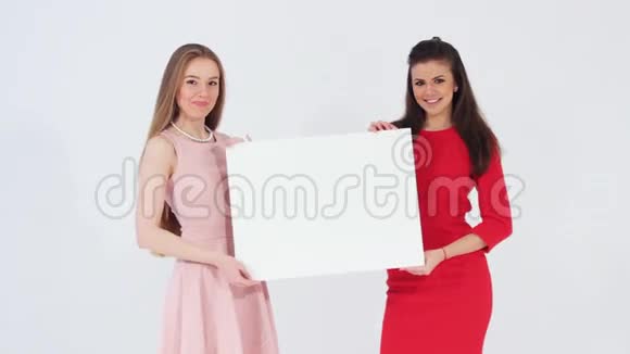 两个微笑的迷人女孩拿着白色空白横幅看着相机视频的预览图