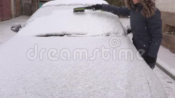 白雪覆盖的汽车旁边有刷子的女人视频的预览图