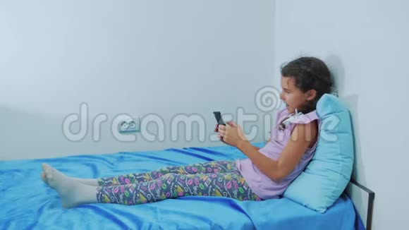 可爱的女孩和狗宠物躺在床上的智能手机肖像小女孩和狗宠物玩网络游戏视频的预览图