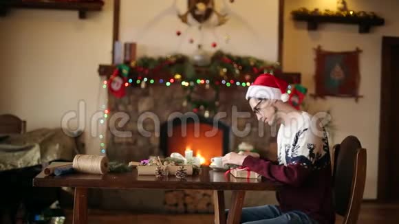 大胡子坐在壁炉旁的礼物上打蝴蝶结戴着纸包圣诞帽装饰着视频的预览图
