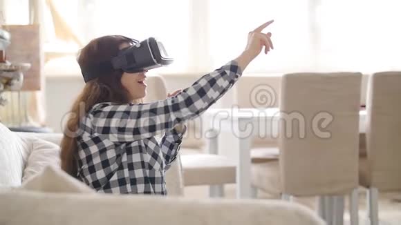 坐在沙发上的虚拟现实耳机中的年轻女子视频的预览图