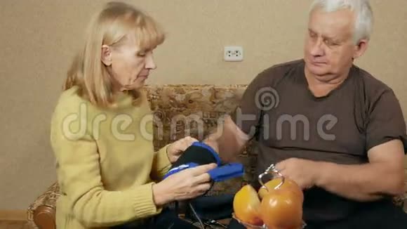高级女性测量一个男人在家里沙发上的血压她戴着你手臂上的袖口听着视频的预览图