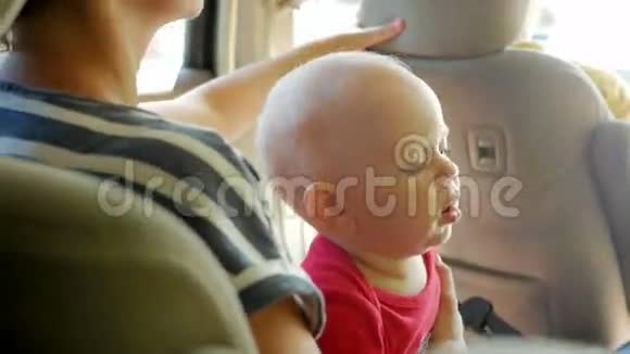 妈妈和孩子一起去汽车后座可爱的1岁小男孩走到妈妈的膝上四处张望视频的预览图