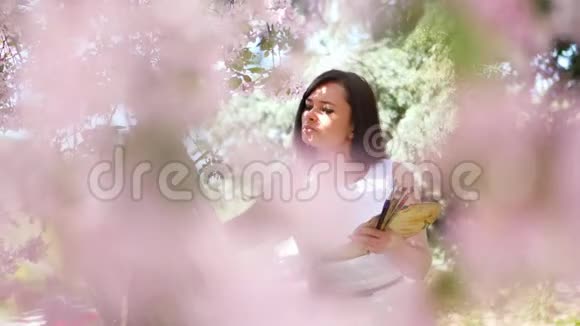 她手里拿着一幅美丽的女画家穿着白色的衣服画着一幅盛开的春苹果园里的鲜花视频的预览图
