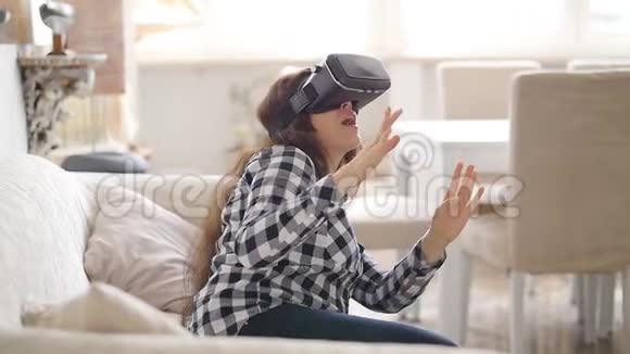 坐在沙发上的虚拟现实耳机中的年轻女子视频的预览图