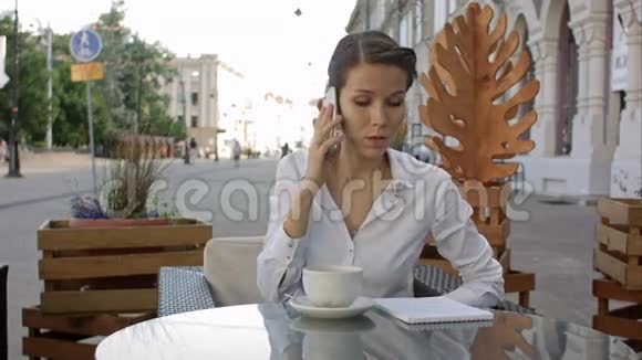 年轻商务女性在户外咖啡馆放松地喝着咖啡打着手机的画像视频的预览图