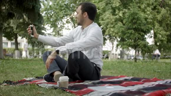 帅哥在公园里拍自拍照片坐在草地上视频的预览图