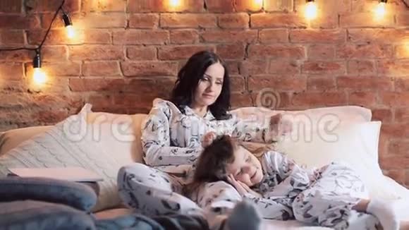 母女俩穿着睡衣坐在床上一起看电视家庭时间视频的预览图