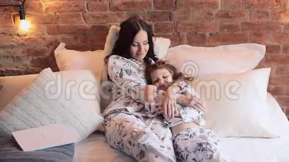 母女俩穿着睡衣坐在床上一起看电视家庭时间视频的预览图