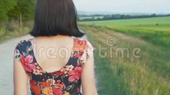 美丽迷人的欧洲女孩留着黑色短发穿着短裙带着鲜花带着砾石沿着道路行走后景视频的预览图