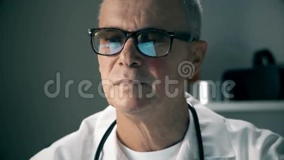 白种人中年医生在他的医疗办公室的笔记本电脑上工作的肖像他调整了眼镜视频的预览图