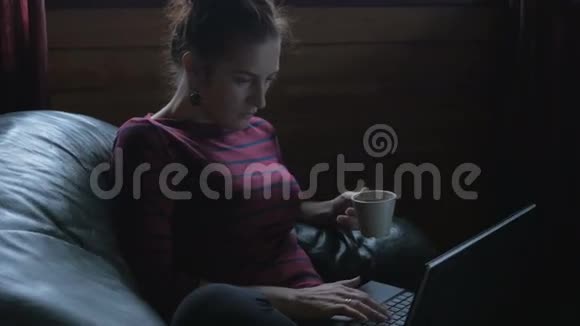 女孩坐在椅子上拿着笔记本电脑喝茶在家工作视频的预览图