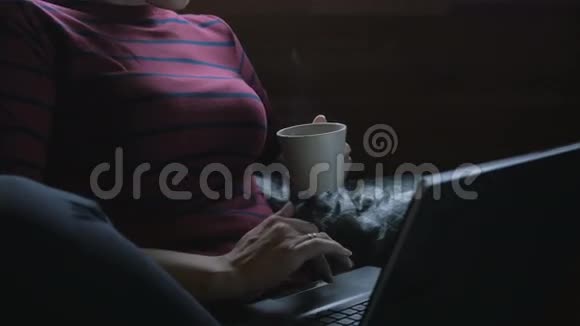 女孩坐在椅子上拿着笔记本电脑喝茶在家工作视频的预览图