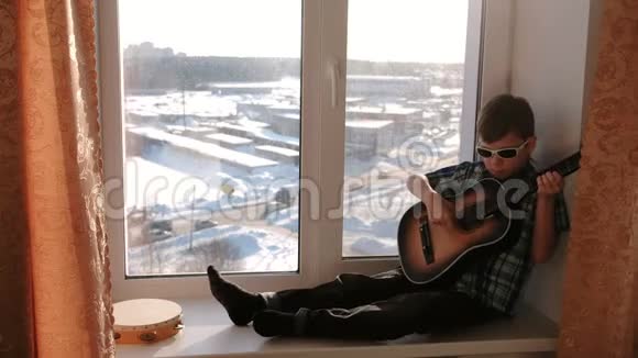 演奏乐器戴太阳镜的男孩坐在窗台上弹吉他视频的预览图