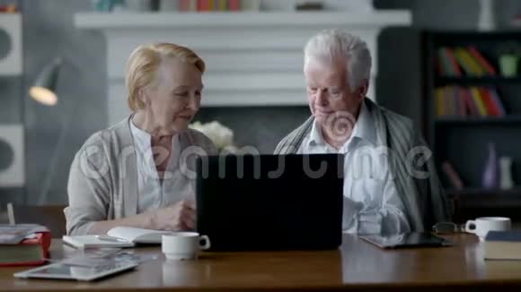 快乐的老年夫妇使用笔记本电脑和智能手机视频的预览图