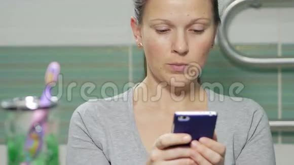 年轻有魅力的女人在浴室里拨打短信她微笑着两只手都集中反应了视频的预览图