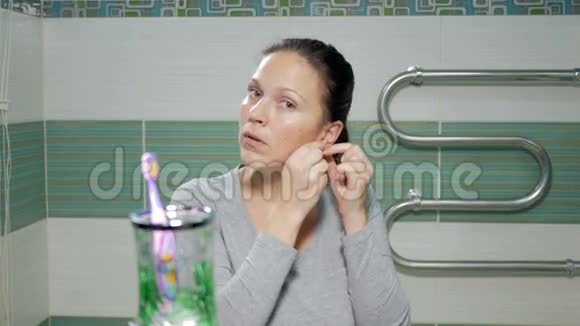 年轻迷人的女人在酒店房间的浴室里戴着珍珠耳环视频的预览图