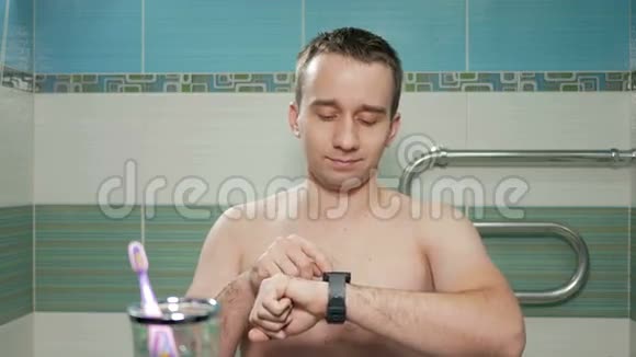 年轻有魅力的男人在酒店房间的浴室里检查智能手表上的信息他读留言然后视频的预览图