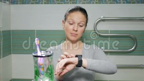 年轻迷人的女人在酒店房间的浴室里的智能手表上查看信息她微笑着发号施令视频的预览图