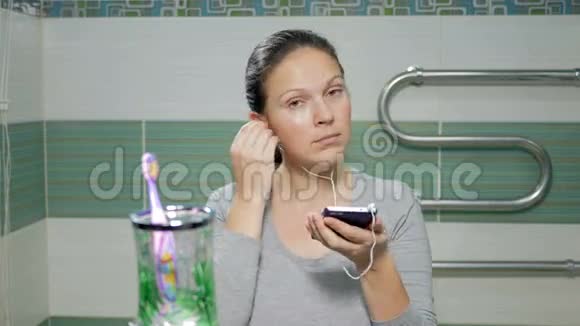 年轻迷人的女人在酒店房间的浴室里用耳机听音乐她在微笑视频的预览图