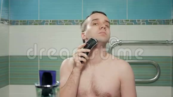 年轻有魅力的男人在浴室刮胡子后用奶油这是电动刮胡子把奶油放在脸上视频的预览图