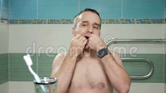 年轻有魅力的男人在浴室里用牙线它彻底清理牙齿之间的洞看着视频的预览图