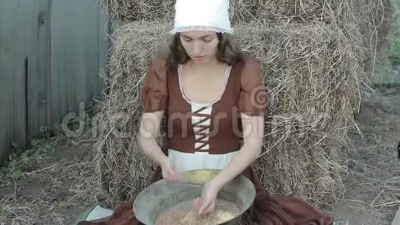 一个穿着乡村服装的漂亮女人坐在干草上把谷物切碎视频的预览图