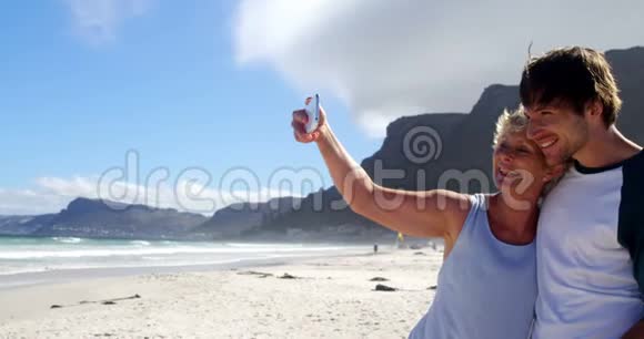 妈妈和儿子在沙滩上用手机自拍视频的预览图