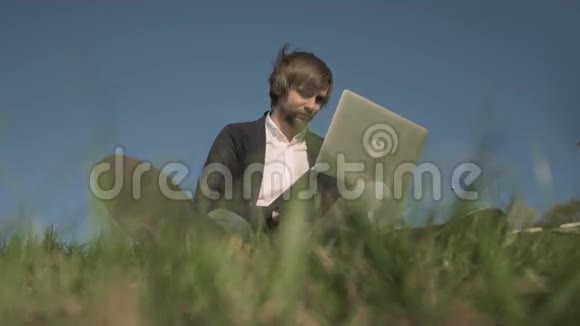 坐在草地上用笔记本电脑看帅哥的底视图视频的预览图
