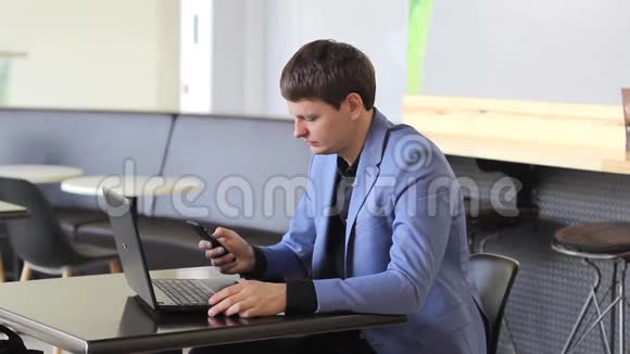 年轻的商人在咖啡馆里用电脑和电话工作视频的预览图
