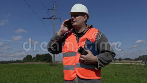 电气工程师在高压线下智能手机上讲话视频的预览图
