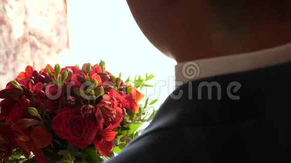 有花的房间穿着夹克和白衬衫的人手里捧着一束美丽的红玫瑰特写镜头美丽美丽视频的预览图