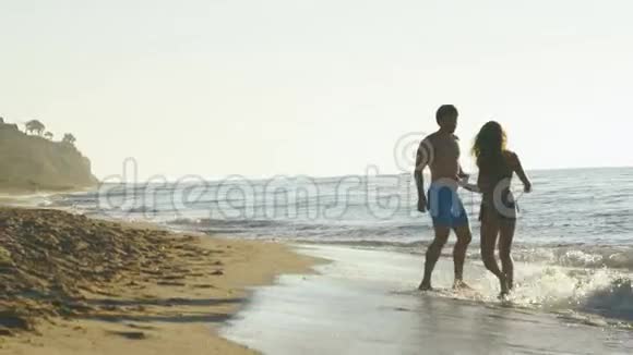 快乐的年轻一对在海边玩冲浪海浪在沙滩上慢动作视频的预览图