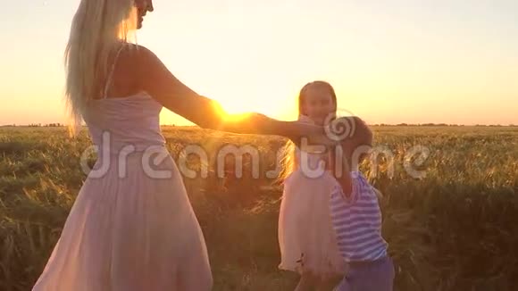 日落时分有两个孩子的女人在田野里转视频的预览图