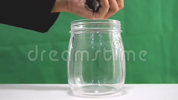 女人把硬币放在玻璃罐子里放在绿色的背景上视频的预览图
