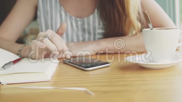 女人在咖啡馆里翻阅智能手机上的照片桌子上放着一杯咖啡和笔记本视频的预览图