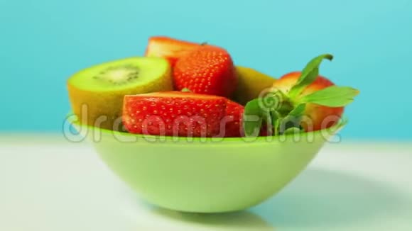 鲜果猕猴桃和切片草莓在蓝色背景上的绿色盘子旋转成一个圆圈视频的预览图