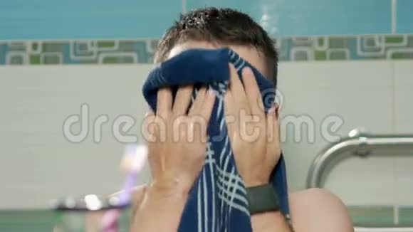 年轻有魅力的男人在酒店洗澡后用毛巾和手在浴室擦拭他的脸他看着视频的预览图