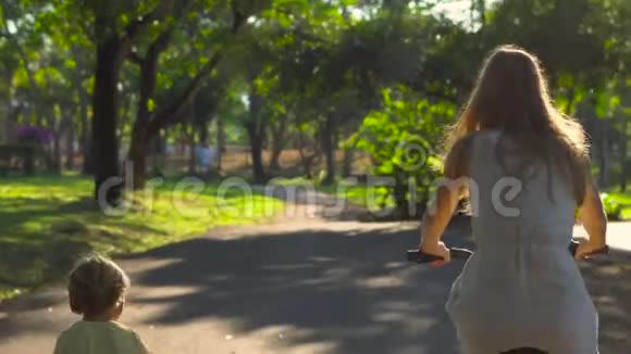 Steadycam在一个热带公园里射杀了一名年轻女子和她的小儿子骑自行车和骑自行车视频的预览图