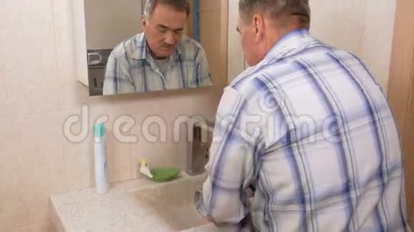 老人在洗澡时用肥皂洗脸术后用水冲洗面部纯洁的概念视频的预览图