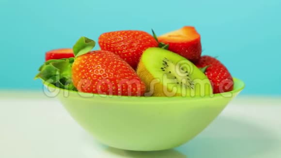 绿色盘子上蓝色背景的鲜奇异果和草莓片旋转成一个圆圈视频的预览图